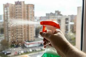 spraying washing liquid on glass of home window photo