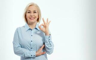 Cheerful smiling blonde business woman lady in blue shirt standing showing Ok gesture looking camera isolated on white background. Selective focus. photo