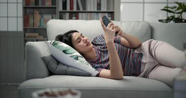 Dolly shot, Young pretty woman to resting with smartphone in hand, she lying on comfortable sofa in living room at home, a small cushion under her head video