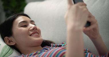 Dolly shot, Close up face of young pretty woman smile with happiness while chatting on smartphone, she lying on comfortable sofa in living room at home a small cushion under her head video