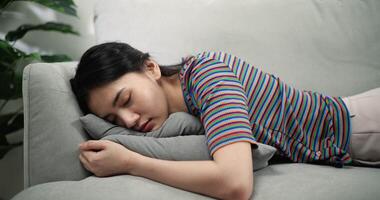 lento movimento tiro di esausto donna addormentato, asiatico giovane femmina chiuso sua occhi e posare giù su il cuscini di il confortevole divano con stanco video