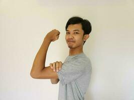 Excited Asian man wearing a grey shirt showing strong gesture by lifting his arms and muscles smiling proudly photo