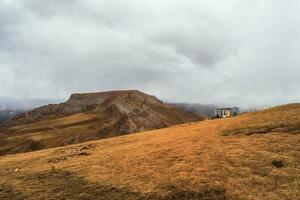 An old tourist wooden house on the edge of a cliff against the backdrop of the majestic autumn plateau of Bermamyt in cloudy weather. photo