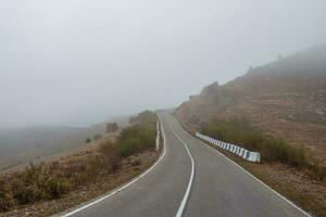 Empty morning mountain highway in a dense fog. Road through a de photo