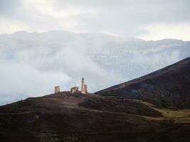 Misty morning in the Caucasus mountains. Medieval tower on foggy mountain slope background. Ingushetia region. photo