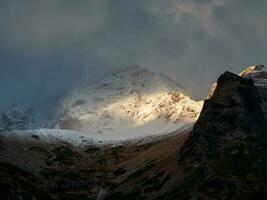 brillante rayo de luz de sol en un glaciar. contrastando montañas a amanecer. Mañana montaña paisaje con Nevado rock en tormenta de nieve. naturaleza antecedentes de rocoso montaña con agudo rock y nublado cielo. foto