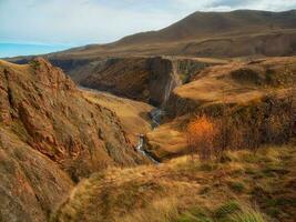 majestuoso otoño montaña paisaje. otoño montaña valle. brillante soleado otoño paisaje con iluminado por el sol oro Valle y devanado río en garganta debajo dramático cielo. foto