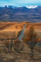 Vertical view of a road stretching into the distance through the picturesque autumn hills. Winding asphalted clean road stretches into the distance to the snow-capped mountains. photo