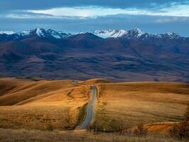 Dawn road stretching into the distance through the picturesque autumn hills. Winding asphalted clean road stretches into the distance to the snow-capped mountains. photo