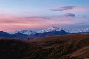 Contrasting mountains at sunset. Purple sunset over majestic mountains. Sunset in magenta tones. Atmospheric purple landscape with a high-altitude snowy mountain valley. photo