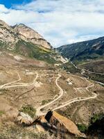 Mountain serpentine in sunlight. Dangerous narrow dirt mountain road through the hills to a high-altitude village. Vertical view. photo