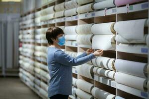 Woman wearing protection facemask choosing wallpaper in hardware store. photo