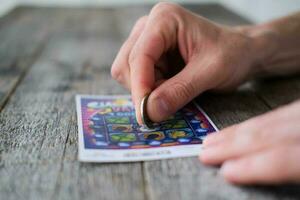 A man is hand erases a protective field in a lottery with a coin on a wooden background. Won. Gambling, addiction. photo