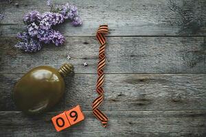 Flask, george ribbon and lilacs on a wooden background. Wooden calendar with date 9 May. Victory Day. Copy space. photo