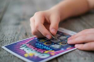 A child is hand erases a protective field in a lottery with a coin on a wooden background. Won. Gambling, addiction. photo