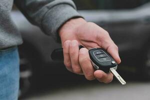 Man in front of the new car and holding keys. Salesman is carrying the car keys delivered to the customer at the showroom with a low interest offer.  Rent, credit, insurance, car purchase. Copy space photo