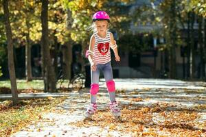 pequeño niña en rodillo patines en un casco montando en el otoño parque. sano estilo de vida concepto. foto