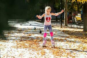 pequeño niña en rodillo patines y tranvía proteccion montando en el otoño parque. sano estilo de vida concepto. foto