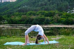 A little girl makes a bridge, bending her back in nature. A flexible child, doing gymnastics exercises. Sports, learning, fitness, stretching, yoga, active lifestyle concepts photo