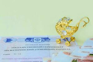 Small gold stroller and document with Russian text State certificate of the Russian Federation for maternal  capital. Russian money of five one thousand rubles. State benefits. Copy space. photo