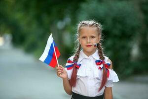 A school child stands on the outdoors and holds the flag of Russia. Little girl with face painting of Russian symbolism. Russian flag day. photo