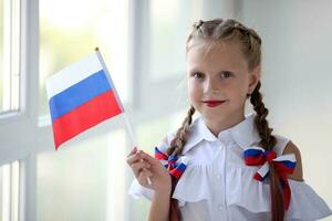 colegio niño soportes y sostiene el bandera de Rusia. pequeño niña con cara pintura de ruso simbolismo. ruso bandera día. foto