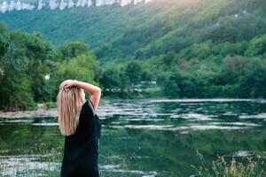 Young woman enjoying the beauty of nature looking at the mountain lake. Adventure travel. A woman stands with raised hands against the backdrop of the lake and mountains. photo