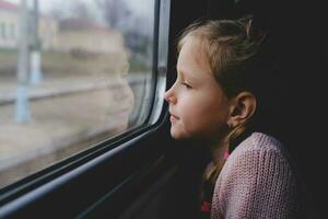 The child is on the train and looks out the window. A little girl travels in a train. photo