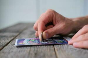 A man is hand erases a protective field in a lottery with a coin on a wooden background. Won. Gambling, addiction. photo