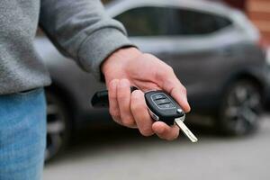 Man in front of the new car and holding keys. Salesman is carrying the car keys delivered to the customer at the showroom with a low interest offer.  Rent, credit, insurance, car purchase. Copy space photo