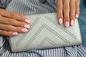 Beautiful pink matte manicure against on the background of a gray bag. Gel silk, oval-shaped nails. photo