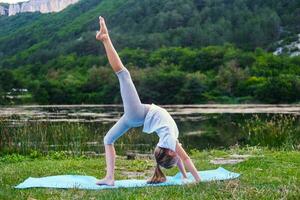 A little girl makes a bridge, bending her back in nature. A flexible child, doing gymnastics exercises. Sports, learning, fitness, stretching, yoga, active lifestyle concepts photo