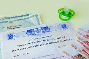 Green pacifier and a document with the text in Russian State certificate of the Russian Federation for maternity capital and a birth certificate. Russian money is five thousand rubles. State benefits. photo