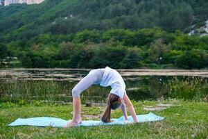 A little girl makes a bridge, bending her back in nature. A flexible child, doing gymnastics exercises. Sports, learning, fitness, stretching, yoga, active lifestyle concepts photo