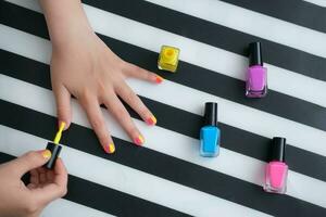 The child sits at the table and paints his nails with bright yellow nail polish. A little girl does a manicure. Beauty salon game. Children's fun. photo