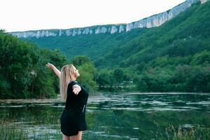 Young woman enjoying the beauty of nature looking at the mountain lake. Adventure travel. A woman stands with raised hands against the backdrop of the lake and mountains. photo