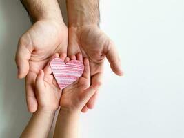 adulto y para niños manos sostener pequeño rojo papel corazón. padres día. familia, amor foto