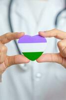 Queer Pride Day and LGBT pride month concept. Doctor hand holding purple, white and green heart shape with Stethoscope for Lesbian, Gay, Bisexual, Transgender, genderqueer and Pansexual community photo