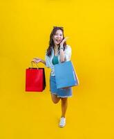 Pretty Asian woman in trendy summer fashion is smiling and holding shopping bags in happiness for discount sale isolated on yellow background for advertising and promotion event concept photo