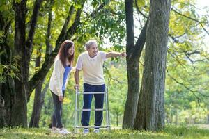 Asian senior man with walker and his daughter walking together in the park looking for beautiful nature and wildlife during summer for light exercise and physical therapy concept photo