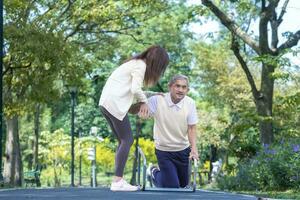 Asian senior man is accidentally fall over in the park due to the slippery road while his niece is lifting him up in injury for elder care and knee surgery recovery concept. photo