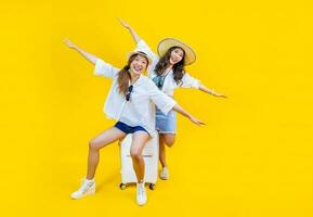 Two Pretty asian women passengers in trendy fashion is exciting to board while carrying her luggage bag in happiness for friendly trip and summer travel vacation isolated on yellow background photo