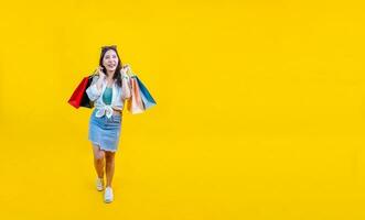 Pretty Asian woman in trendy summer fashion is smiling and holding shopping bag in happiness for discount sale isolated on yellow background for advertising and promotion event concept photo