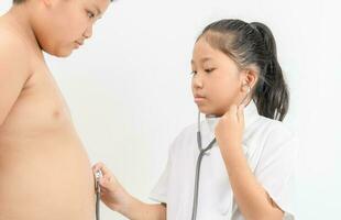 Little doctor is checking fat boy stomach with a stethoscope on white photo