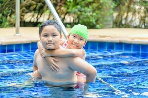 hermano participación hermana en su espalda en nadando piscina foto