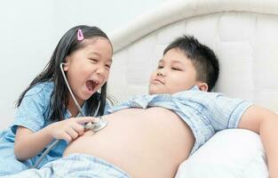 Cute sister playing check big stomach by stethoscope photo