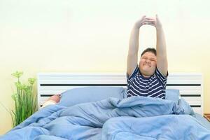 Fat boy stretching in bed after waking up, photo