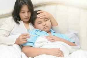 Mother checking temperature of her sick son with high fever photo