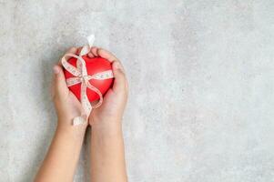 kid holding a red heart shape on marble table. photo