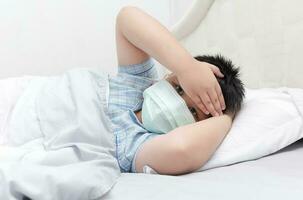 sick boy with hygienic mask lie down on bed photo